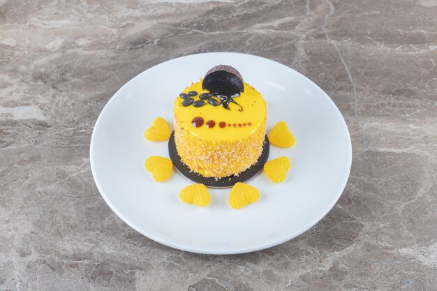 Free photo lemon flavor coating on a small cake surrounded with jelly sweets on a platter on marble surface