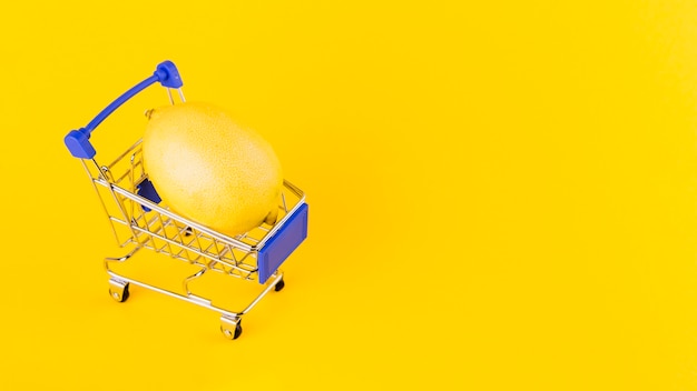 黄色の背景に対してショッピングカート内のレモン
