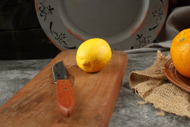 Free photo a lemon and a knife on a wooden board.