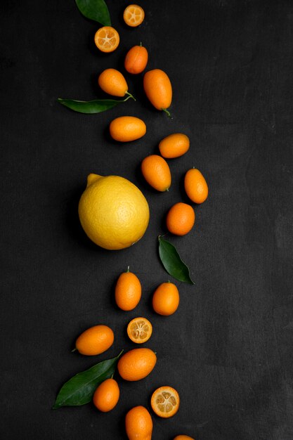 Lemon and kumquats decorated with leaves on black surface