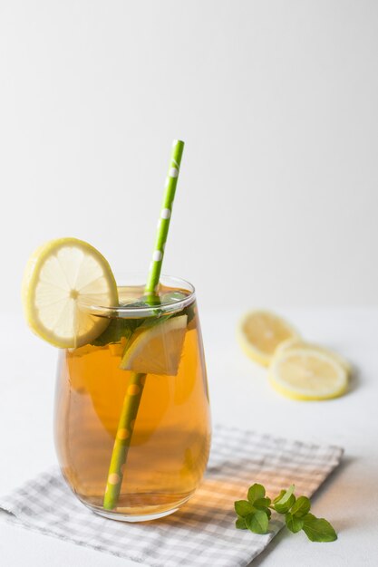 Lemon and mint herbal tea glass with green drinking straw on folded tablecloth against white backdrop