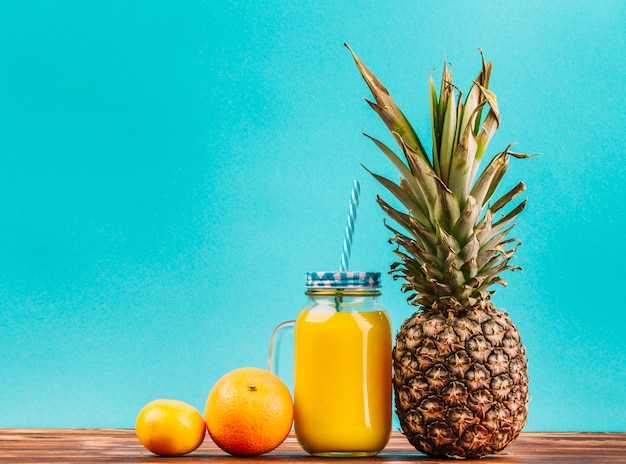 Lemon; orange fruit; pineapple and juice mason jar with straw against turquoise background