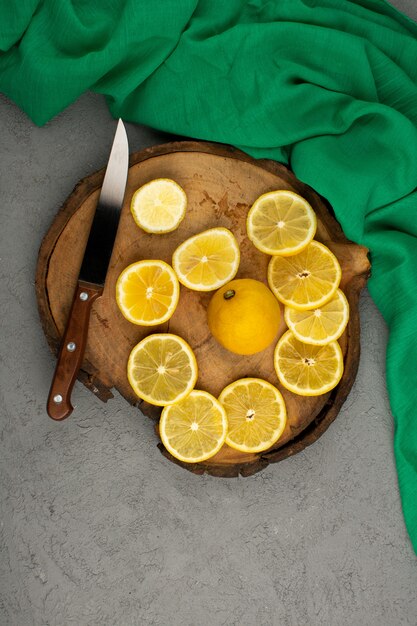 グレーの緑のティッシュの周りの茶色の木製の机の上のレモンの新鮮な酸っぱいジューシーな作品