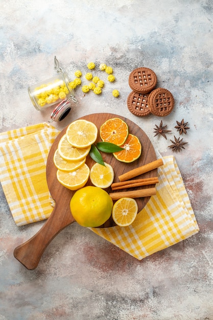 Ломтики лимона, корицы и лайма на деревянной разделочной доске и печенье на белом столе