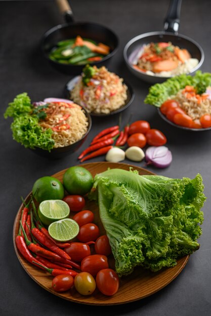 Lemon slices, shallots, garlic, tomatoes, lettuce and peppers on a wooden plate on a black cement floor.