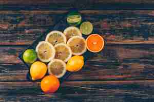 Free photo lemon slices with oranges and green lemon flat lay on a cutting board and dark wooden background space for text