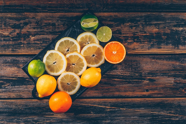 Ломтики лимона с апельсинами и зеленым лимоном положите на разделочную доску и темный деревянный фон для текста