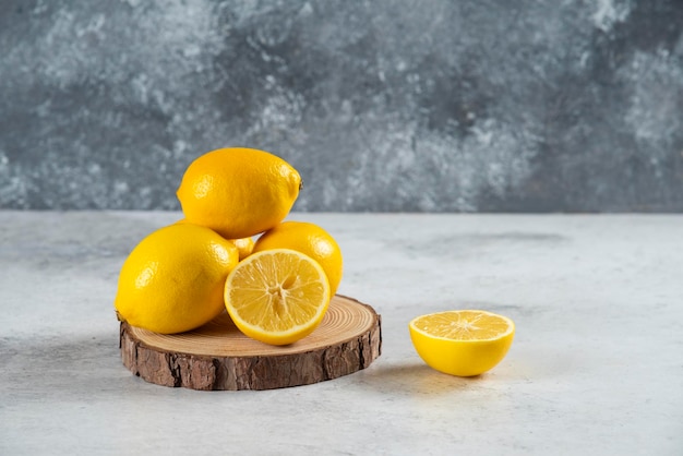 Lemon slices in wooden board with a whole lemon on marble background.