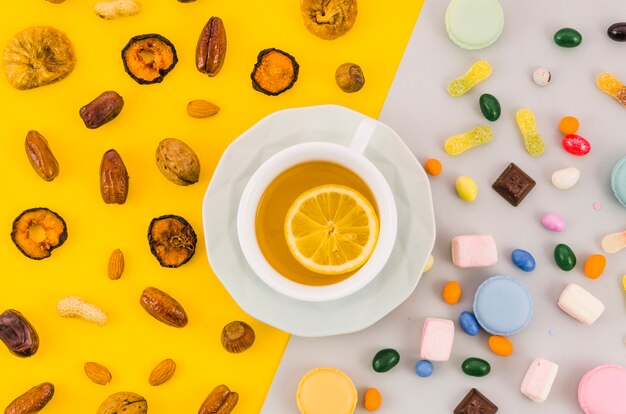 Lemon tea cup with dried fruits and candies on yellow and white dual background