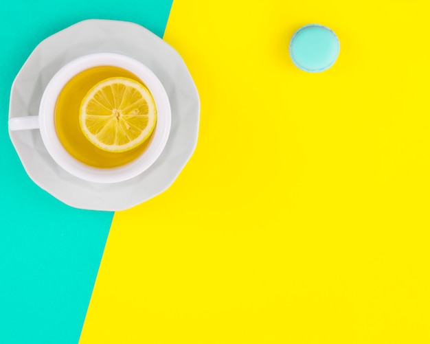 Lemon white tea cup and saucer with macaroon on turquoise and yellow backdrop