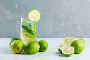Free photo lemonade in a glass with lemons, herbs side view on white and plaster