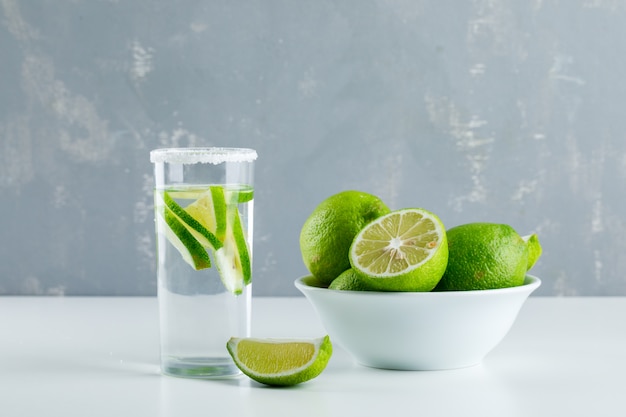 Limonata in un bicchiere con vista laterale di limoni su bianco e gesso