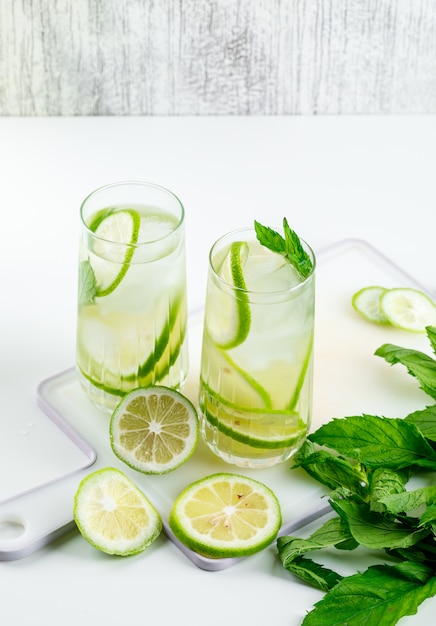 Lemonade in glasses with lemon, basil, cutting board high angle view on white and grungy