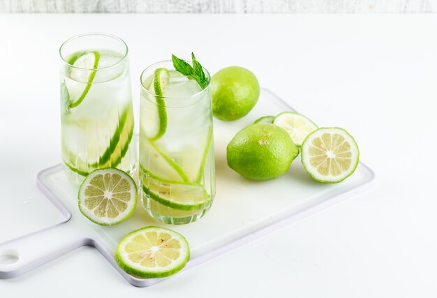 Lemonade in glasses with lemon, basil, cutting board high angle view on white and grungy