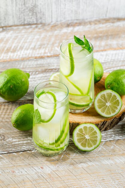 Lemonade in glasses with lemon, basil, cutting board high angle view on wooden and grungy