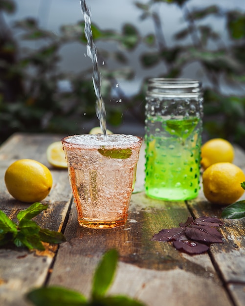 Lemonade and ingredients in glass and jar on wooden and yard table, side view.