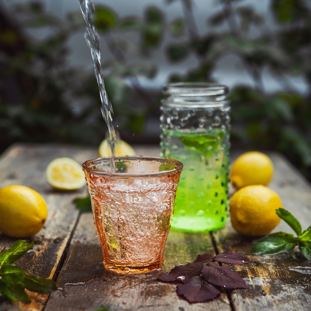 Lemonade and ingredients in glass and jar on wooden and yard table. side view.