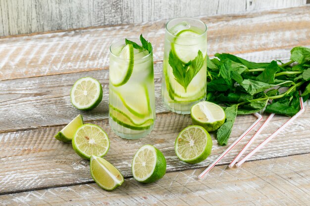 Lemonade with lemon, basil, straws in glasses on wooden and grungy, high angle view.