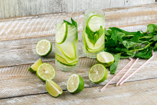 Lemonade with lemon, basil, straws in glasses on wooden and grungy, high angle view.