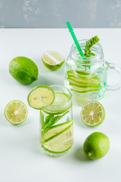 Lemonade with lemon, herbs, straw in glass and mason jar on white and grey, high angle view.