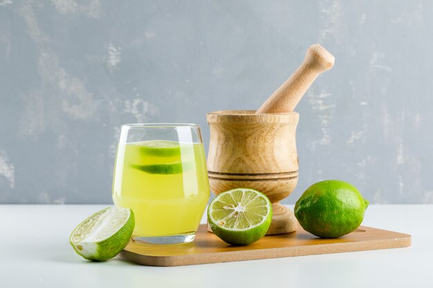 Лимонад с лимоном, ступкой и пестиком, разделочная доска в стакане на белом и гипс,
