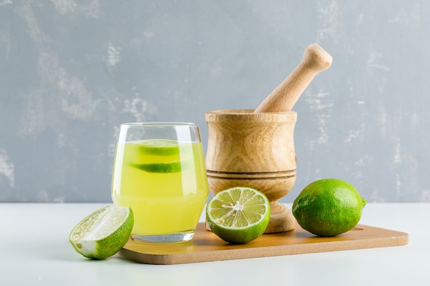 Lemonade with lemon, mortar and pestle, cutting board in a glass on white and plaster,