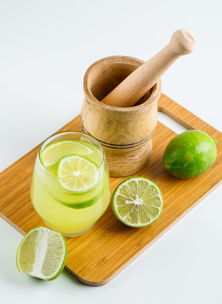 Lemonade with lemon, mortar and pestle in a glass on white and cutting board, high angle view.