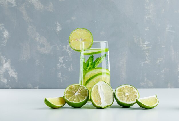 Lemonade with lemons, herbs in a glass on white and plaster,