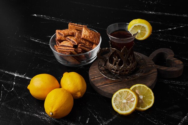 Lemons isolated on a black surface with tea and pastries.
