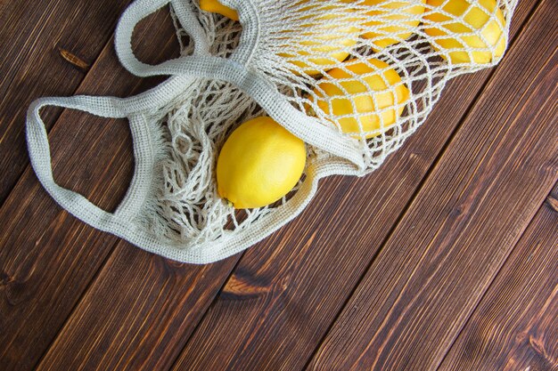 Lemons in a mesh bag on a wooden table. flat lay.