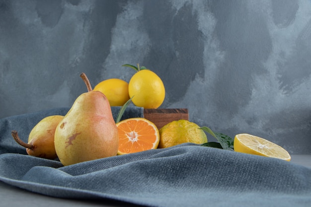 Lemons, tangerines and pears on a piece of fabric on a wooden board, on marble 