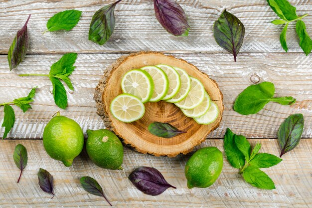 Lemons with basil leaves on wooden and cutting board, flat lay.