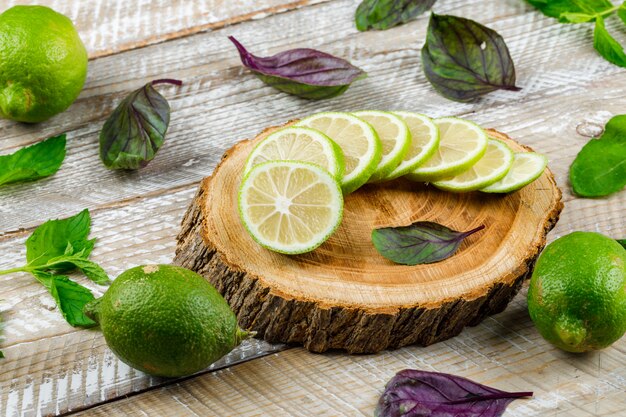 Lemons with basil leaves on wooden and cutting board, high angle view.