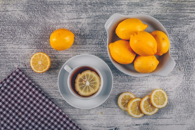 Lemons with cloth, tea and slices in a bowl and on gray wooden background, top view.