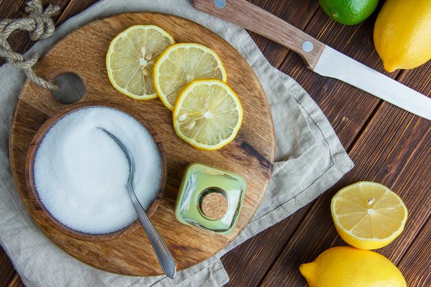 Lemons with drink, cutting board, salt, knife flat lay on wooden and kitchen towel