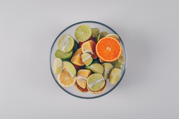 Lemons with green lemons and orange in a bowl on white background, top view.