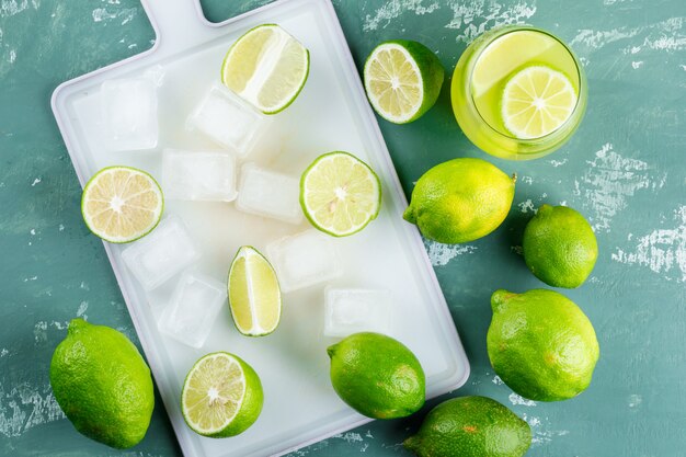 Lemons with ice cubes, lemonade flat lay on plaster and cutting board