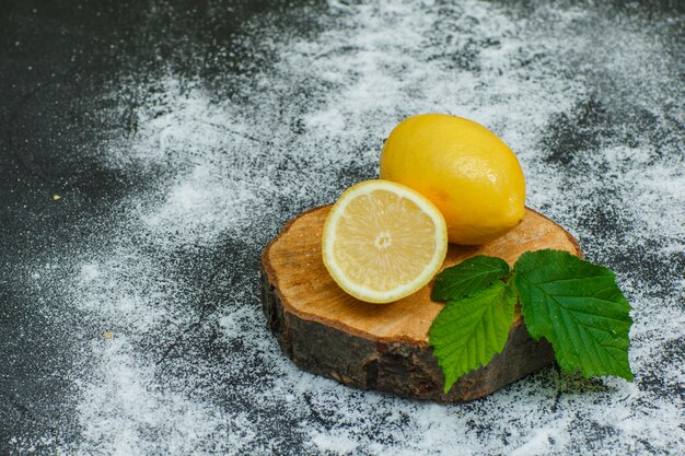 Lemons with leaves and dry cinnamon high angle view on wood slice and dark