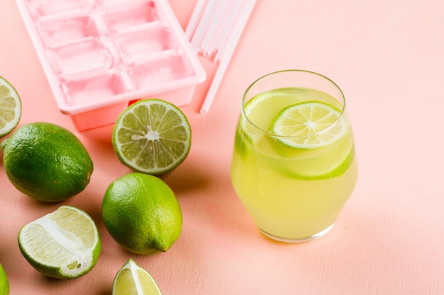 Lemons with lemonade, ice tray, straws high angle view on a pink