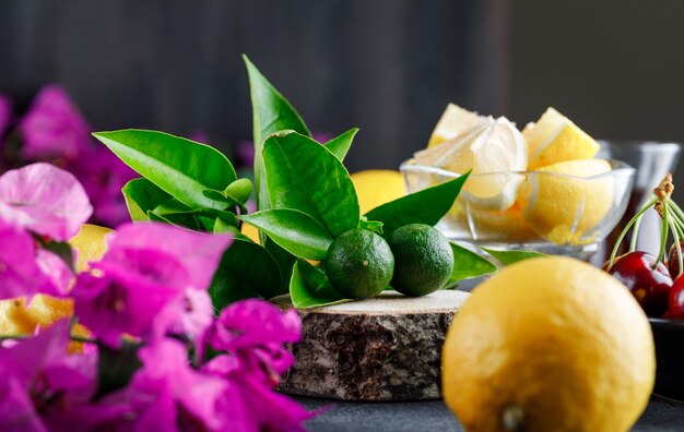 Lemons with slices, flowers, wooden board, cherries close-up on a grey surface