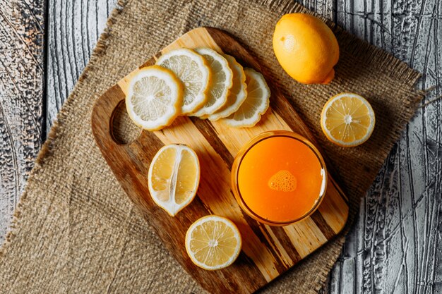 Lemons with slices and juice top view on a cutting board, cloth and wooden background