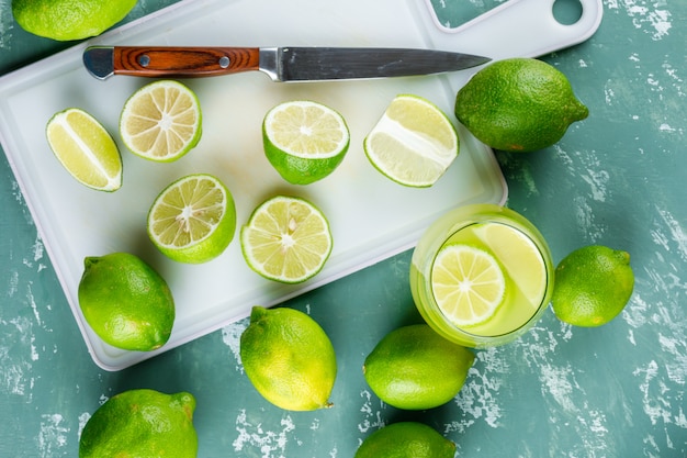 Lemons with slices, knife, lemonade flat lay on plaster and cutting board