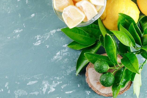 Lemons with slices, leaves, wooden board top view on a plaster surface