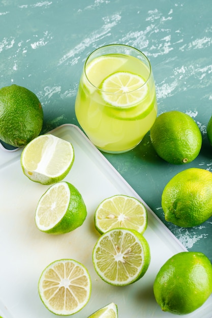 Free photo lemons with slices, lemonade high angle view on plaster and cutting board