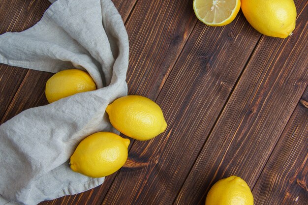 Lemons on wooden and kitchen towel, flat lay.