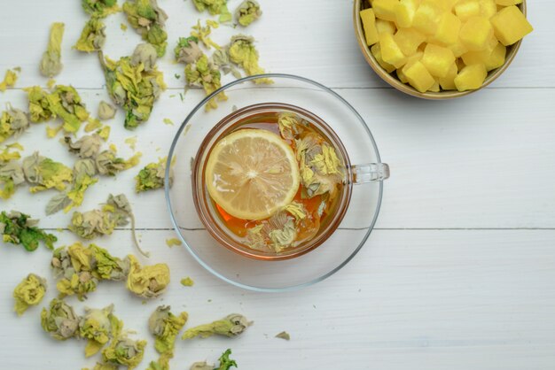 Lemony tea in a cup with dried herbs, sugar cubes flat lay on a wooden surface