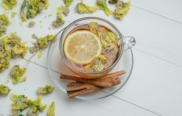 Lemony tea with dried herbs, cinnamon sticks in a cup on wooden surface, high angle view.