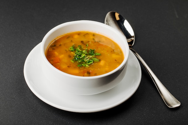 Lentil soup with mixed ingredients and herbs in a white bowl with a spoon.