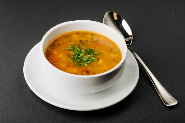 Lentil soup with mixed ingredients and herbs in a white bowl with a spoon.