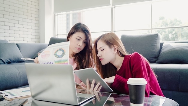 Lesbian Asian couple using laptop making budget in living room at home, sweet couple enjoy love mome